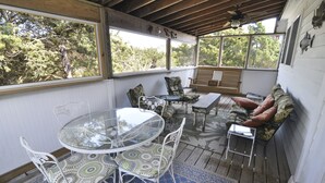 En inglasad veranda med ett glasbord och stolar, en träbänk och en soffa med mjuka kuddar.