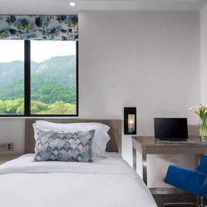 A hotel room with a bed, a desk with a laptop, a chair, and a window with a view of greenery. - I Noble Hotel (Shenzhen)