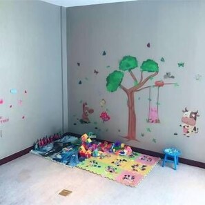 Um quarto infantil com um tapete de brincadeira colorido, um banquinho pequeno azul e decorações nas paredes, incluindo uma árvore e animais.