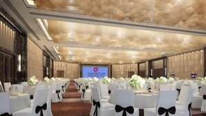 A conference room with rows of white chairs, a large screen at the front, and a patterned carpet.