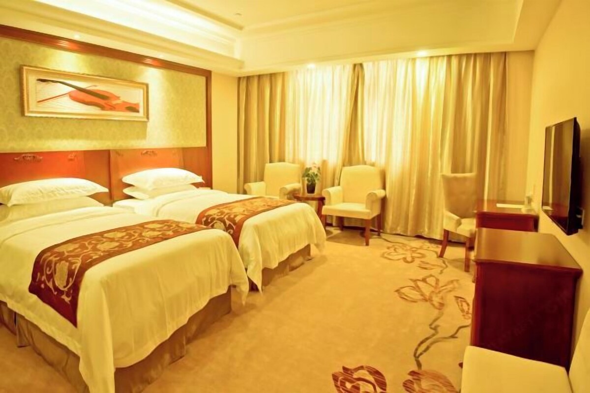 A hotel room with two beds, a TV, a desk, and a chair.