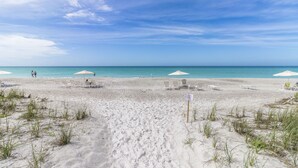 A beach with white umbrellas and lounge chairs, a clear sky, and the ocean in the background. - Gulf-Front Luxury: 2BR Beachplace Condo on Longboat Key Unit 9-103 by RVA (Longboat Key)