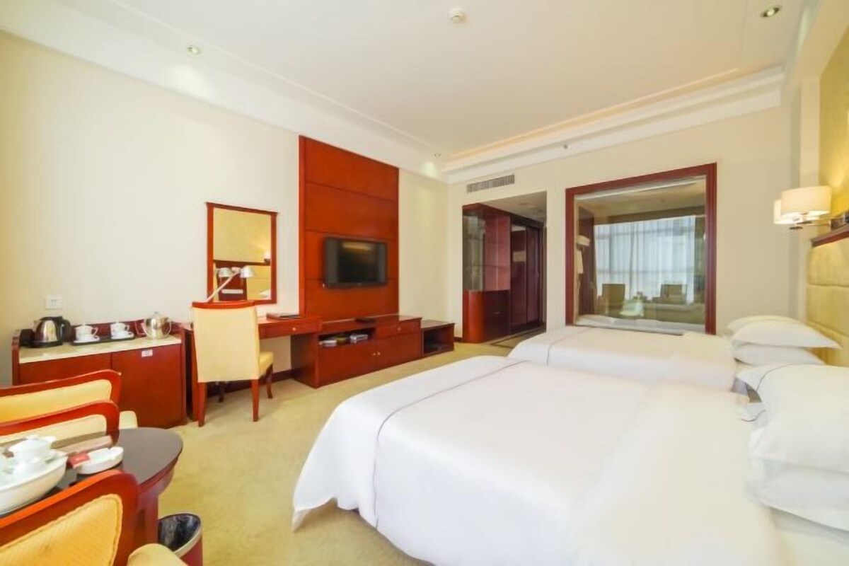 Una habitación de hotel con una cama, un escritorio con silla, un televisor y un espejo.