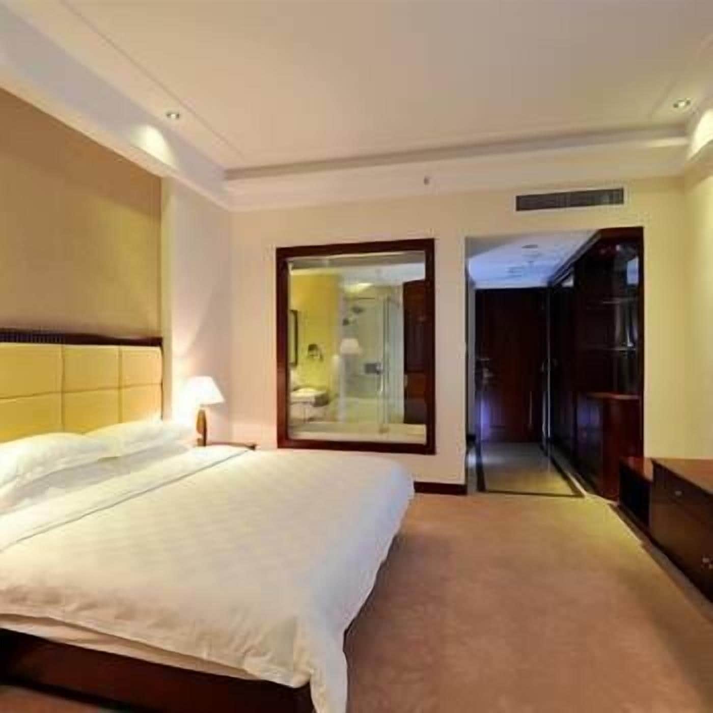 A hotel room with a bed, a nightstand, a mirror, and a wardrobe.