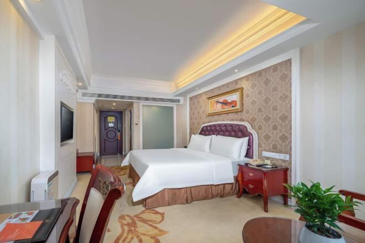 A hotel room with a bed, a TV, a desk, and a chair.