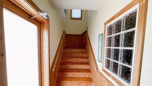 Eine Holztreppe mit Handlauf, ein Fenster mit Dekorglas und eine Tür mit Lichtschalter.