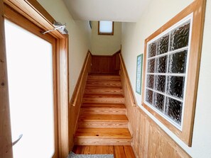 A wooden staircase with a handrail, a window with decorative glass, and a door with a light switch.