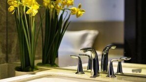 Une salle de bain avec un lavabo blanc, deux robinets et un vase rempli de fleurs jaunes.