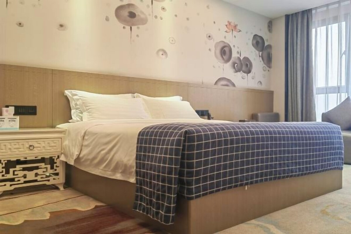 A hotel room with a bed, nightstands, a wall clock, and a window with curtains.