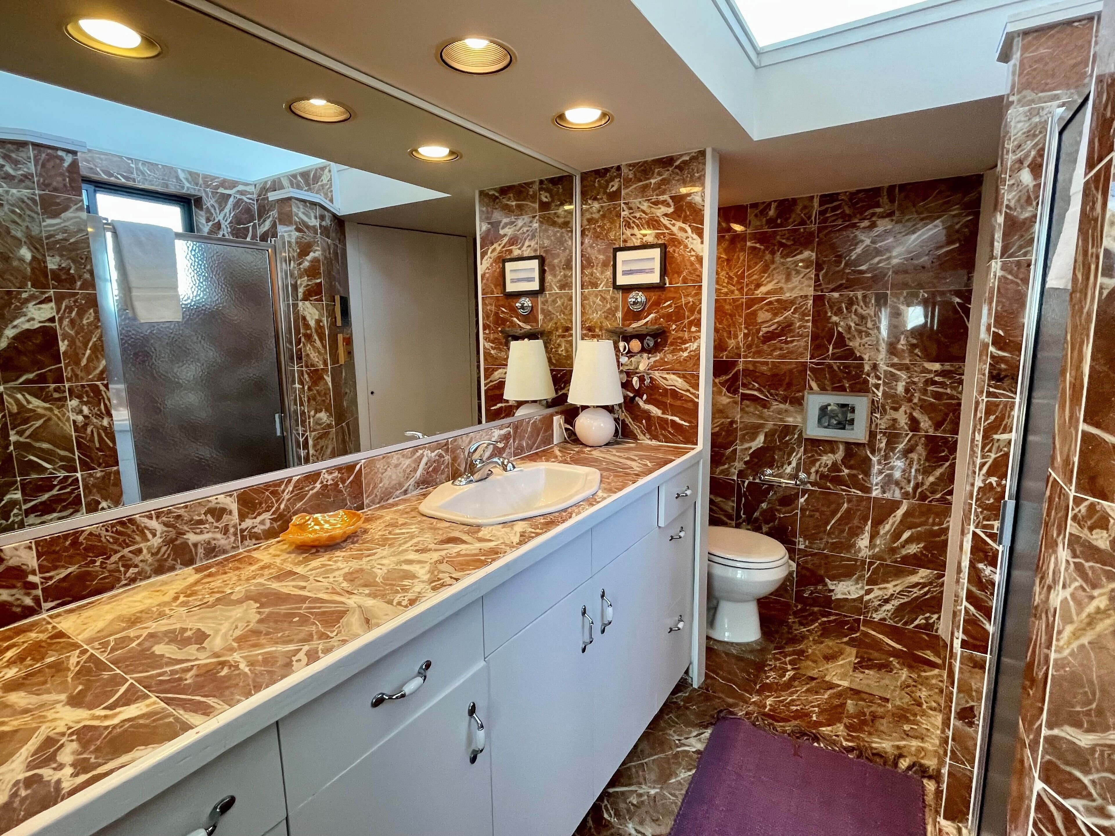 Une salle de bain avec un meuble-lavabo en marbre, un évier, un miroir et des toilettes.