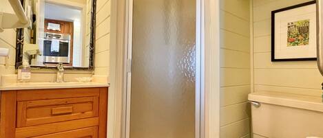 A bathroom with a wooden vanity, a glass shower enclosure, and a toilet.