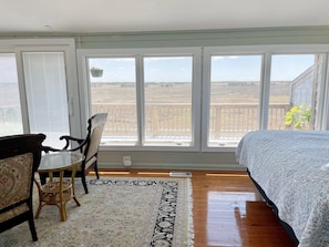 Una habitación con cama, una mesa, dos sillas y un ventanal con vistas al campo.