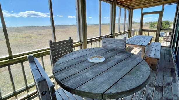 Een houten terras met een ronde tafel en bankjes, met uitzicht op een veld.