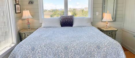A bedroom with a large bed, two windows, and a view of the outdoors.