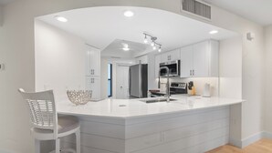 A modern kitchen with white cabinetry, a large island with a sink, and a built-in oven. - 🌺Bandy Beach A101: Brand-New Beachfront Oasis w/ Dual Kings & Pool🌴 (Sanibel)