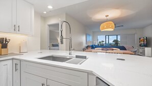 A modern kitchen with a large island, a built-in sink, and a dining area with a view of the ocean. - 🌺Bandy Beach A101: Brand-New Beachfront Oasis w/ Dual Kings & Pool🌴 (Sanibel)