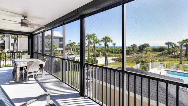 A balcony with a table and chairs, a ceiling fan, and a view of a swimming pool and greenery. - 🌺Bandy Beach A101: Brand-New Beachfront Oasis w/ Dual Kings & Pool🌴 (Sanibel)