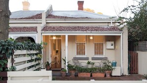 A two-story house with a covered porch, potted plants, and a white fence.