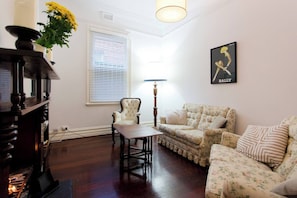 Una sala de estar con un sofá floral, una mesa de centro de madera, un sillón blanco, una chimenea y un cuadro colgado en la pared.