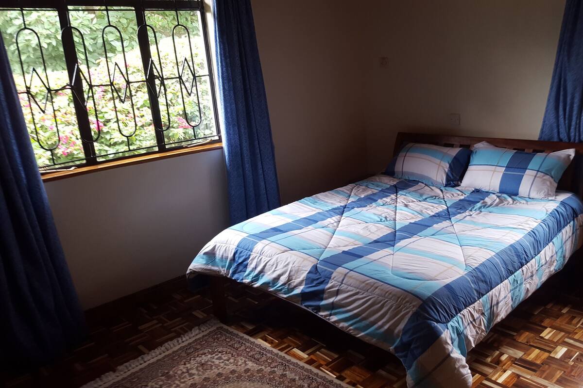 A bedroom with a wooden floor, a bed with a blue and white quilt, and a window with a metal grill.