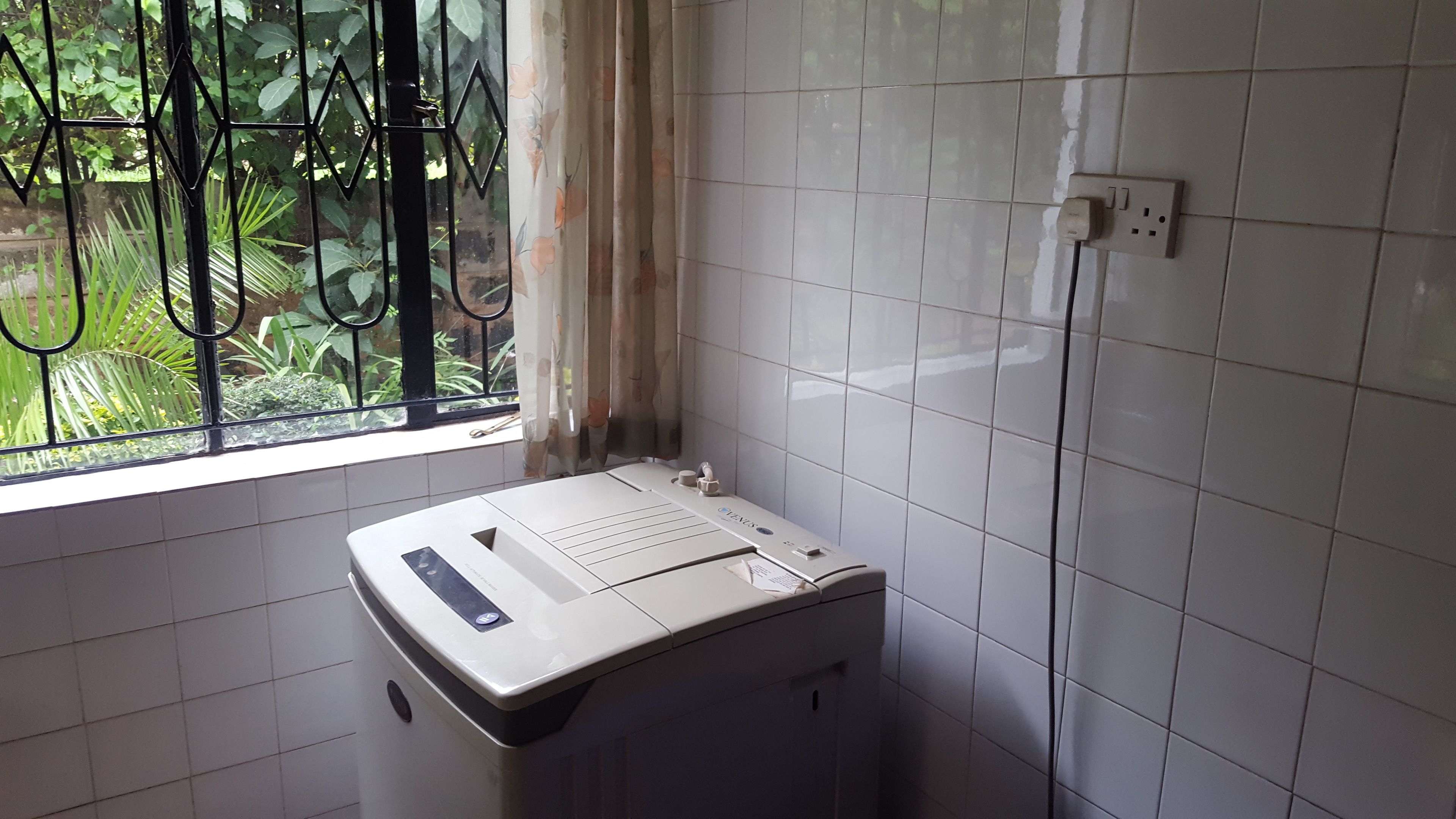 A compact room with a window, a white tiled wall, and a white washing machine.