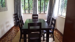 A dining area with a rectangular table surrounded by chairs, a patterned floor, and windows with curtains. - Milima 7 (Nairobi)