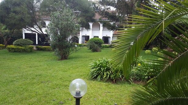 A well-maintained garden with a white building featuring arched windows and a tiled roof. - Milima 7 (Nairobi)