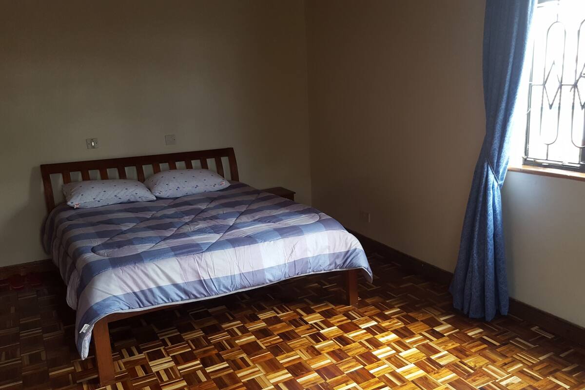 A room with a wooden bed, a patterned bedspread, and a window with metal bars.