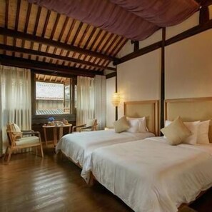Habitación de hotel con dos camas, techo de madera, ventana con cortinas, una silla y una mesita.
