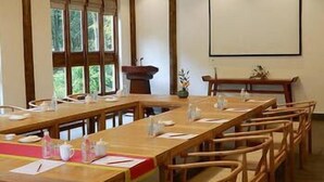 A conference room with long tables and chairs, a projector screen, and a window with a view of trees. - Kaiyuan Hotel · Seabirds (Hangzhou)
