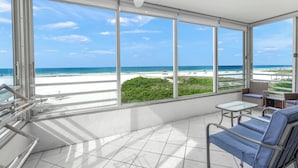 A room with large windows overlooking a beach, a ceiling fan, and a seating area with a table. - Island House Beach Resort 3N (Siesta Key)