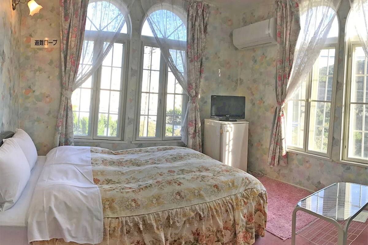 A bedroom with a bed, a TV, and a window with curtains.