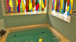 A bathtub with a greenish water color, surrounded by tiled walls and a colorful stained glass window. - Pension Smile Again (Shimoda)