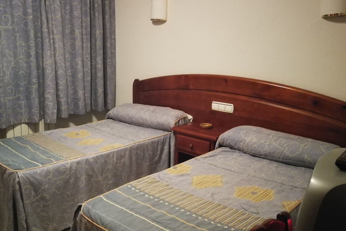 A room with two single beds, a wooden headboard, a bedside table, and a wall-mounted light fixture.