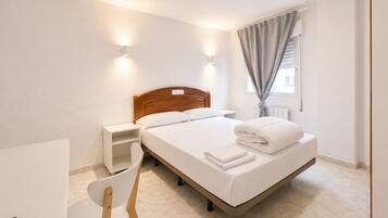 A hotel room with a bed, bedside table, chair, and a window with curtains.