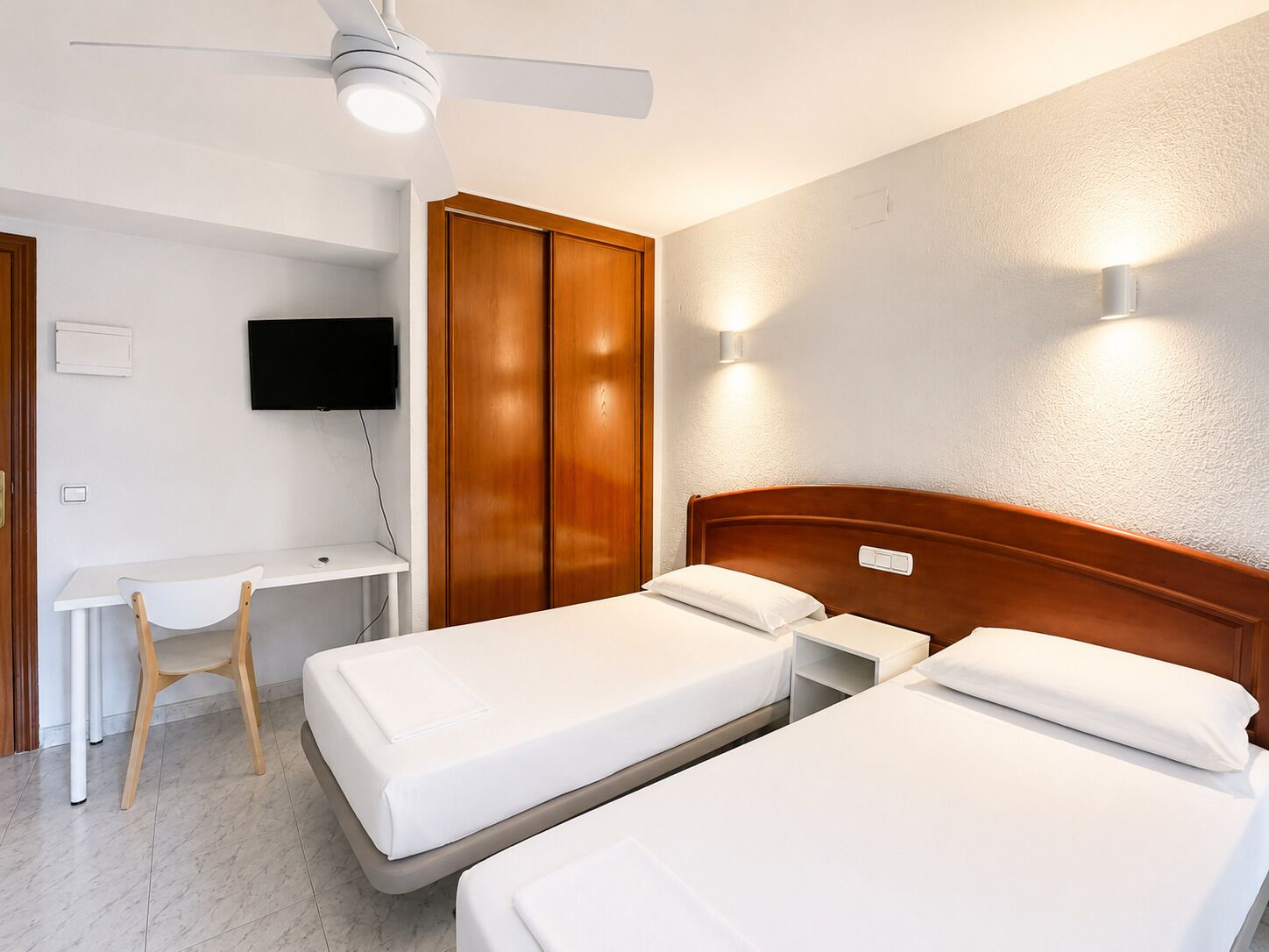Habitación de hotel con dos camas, un escritorio, una silla, un televisor y un armario.
