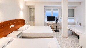 Una habitación de hotel con una cama, un escritorio con una computadora, una silla y un ventilador de pie.
