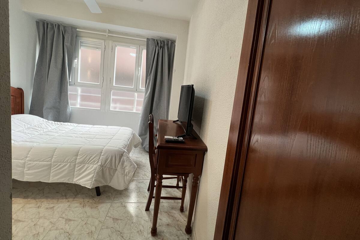 A bedroom with a bed, a desk with a television, and a window with curtains.