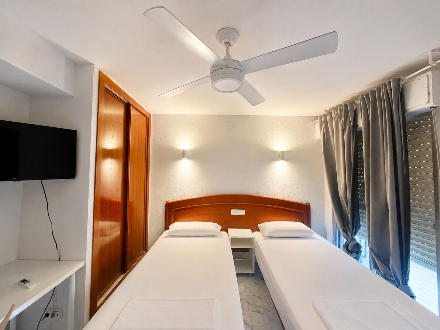 Una habitación de hotel con una cama individual, un escritorio, un televisor y un ventilador de techo.