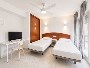Habitación de hotel con cama, escritorio, silla, televisor, armario y ventilador de techo.