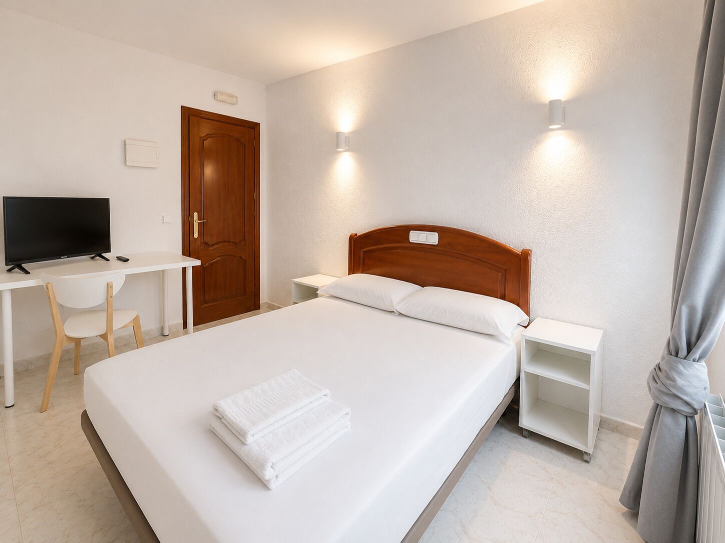 Habitación de hotel con cama, escritorio, televisión y armario.