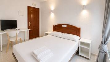 Habitación de hotel con cama, escritorio, televisión y armario.
