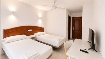 A hotel room with two beds, a desk, a chair, a television, and a ceiling fan.