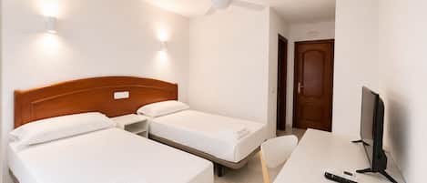 Habitación de hotel con dos camas, un escritorio, una silla, un televisor y un ventilador de techo.