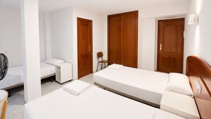 Una habitación de hotel con dos camas, una silla, un escritorio y un ventilador.