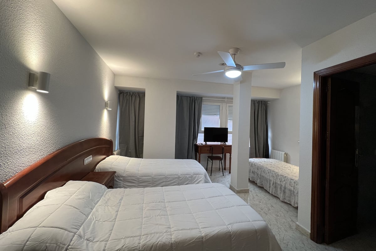 A hotel room with two beds, a desk with a chair, a ceiling fan, and a television.