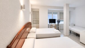 Habitación de hotel con dos camas, un escritorio con computadora y una ventana con persianas.