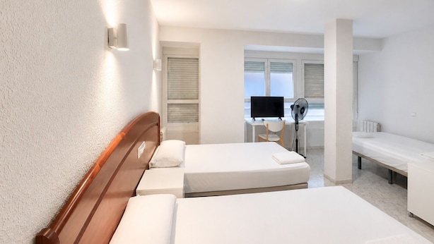A hotel room with two beds, a desk with a computer, and a window with blinds. - Hostal La Embajada (Talavera de la Reina)