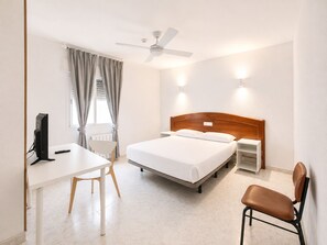 A hotel room with a bed, a desk, a chair, a computer, a ceiling fan, and wall-mounted lights. - Hostal La Embajada (Talavera de la Reina)