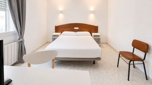 A hotel room with a bed, bedside tables, a chair, a desk, a ceiling fan, and a window with curtains. - Hostal La Embajada (Talavera de la Reina)